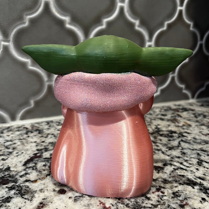 May include: A pink and green figurine of a character from the Star Wars franchise. The figurine is made of plastic and has a shiny finish.