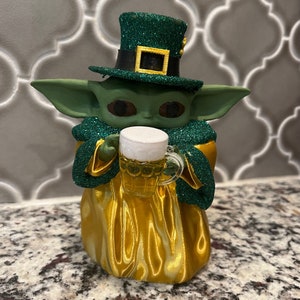 May include: A green and gold figurine of a character wearing a green leprechaun hat and holding a glass of beer.