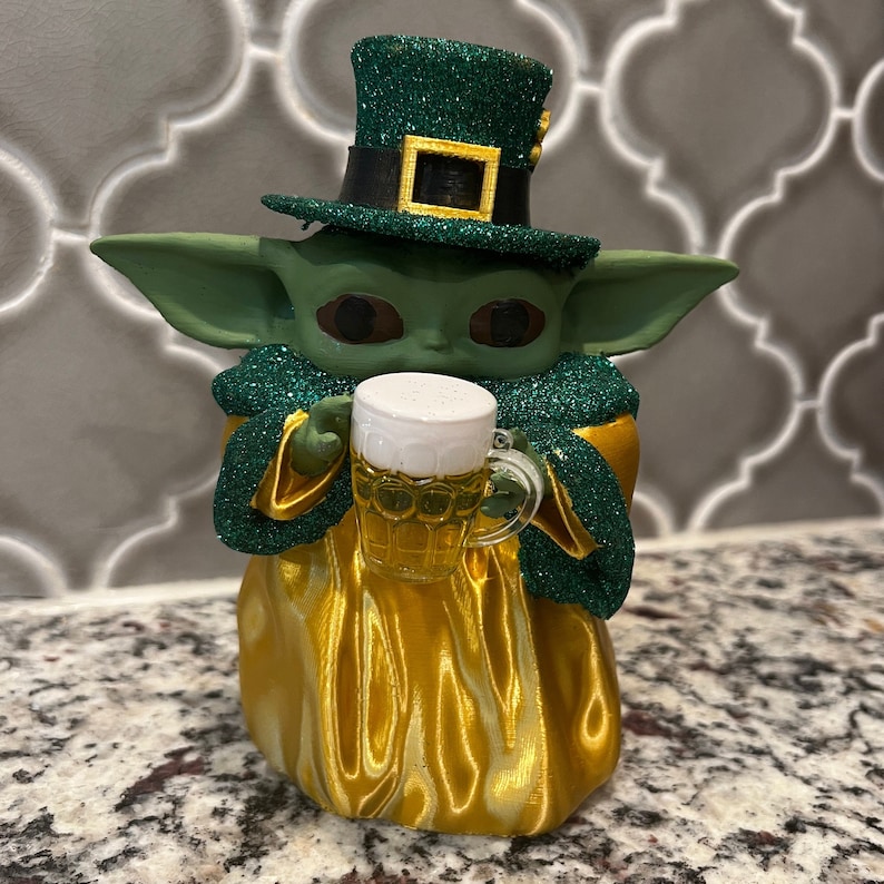 May include: A green and gold figurine of a character wearing a green leprechaun hat and holding a glass of beer.