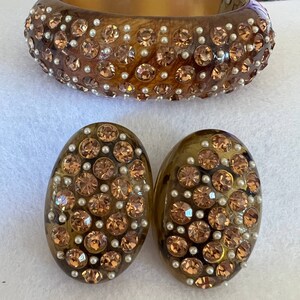 May include: A set of brown tortoise shell earrings and a matching bracelet. All three pieces are adorned with small, sparkling brown rhinestones and white pearls.