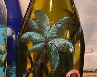 Puede incluir: Botella de vidrio decorativa pintada a mano con una escena tropical. La botella muestra una palmera y dos flamencos rosas. La parte superior está envuelta con hilo y alambre de cobre. La botella mide unos 30 cm de alto.