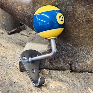 Peut inclure: Un crochet mural en métal avec un design de boule de billard numéro 10. La boule est jaune et bleue avec le numéro 10 en blanc. Le crochet a un bras courbé et une plaque de montage pour accrocher des objets.