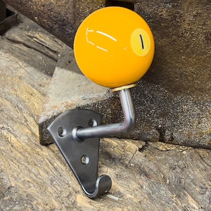 Peut inclure: Un crochet en forme de boule de billard jaune avec un numéro un noir, monté sur un support métallique. Le crochet est fixé à un bras métallique incurvé et à un support métallique foncé avec trois trous de montage. Le crochet est conçu pour suspendre des objets.