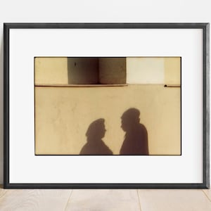 May include: A black and white photograph of two shadows of people talking against a light yellow wall.
