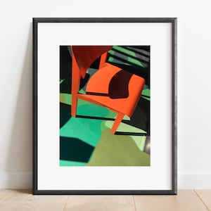 Pode incluir: Uma cadeira laranja brilhante com um chão estampado verde e castanho por baixo. A cadeira está em foco e o chão está desfocado.