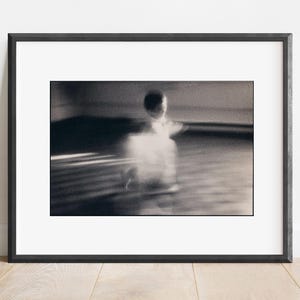 Puede incluir: Una fotografía en blanco y negro de una figura borrosa con un vestido blanco, capturada en movimiento.