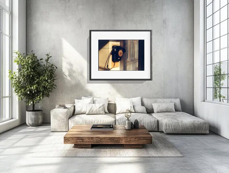 May include: A framed wall art print featuring a black vintage wall-mounted telephone with a circular dial and a hanging handset, displayed in a room with a light gray sofa, a wooden coffee table, and a potted plant.