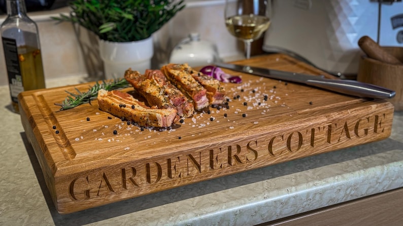 Puede incluir: Una tabla de cortar de madera grande con las palabras "Gardeners Cottage" grabadas en la parte delantera. La tabla est&aacute; cubierta de sal y pimienta y tiene varios trozos de carne cocida encima.