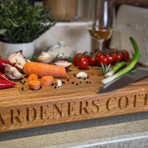 Puede incluir: Una tabla de cortar de madera con las palabras "GARDENERS COTTAGE" grabadas en la parte delantera. La tabla est&aacute; cubierta con varias verduras, incluyendo pimientos rojos, cebollas verdes, zanahorias y tomates.