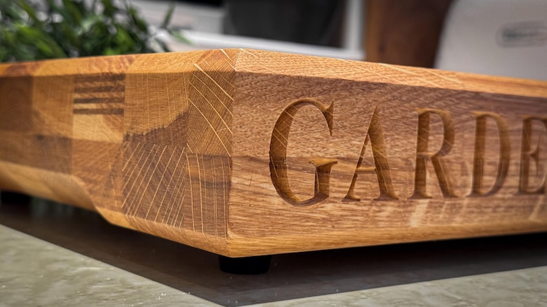 Puede incluir: Una tabla de cortar de madera con un acabado natural y la palabra "GARDEN" tallada en la superficie.