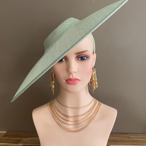 May include: A light green hat with a wide brim, displayed on a mannequin head. The hat is paired with gold-toned earrings and a layered necklace. The mannequin has a fair complexion and is set against a neutral background.