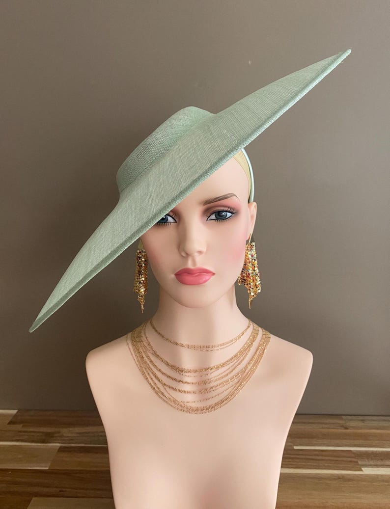 May include: A light green hat with a wide brim, displayed on a mannequin head. The hat is paired with gold-toned earrings and a layered necklace. The mannequin has a fair complexion and is set against a neutral background.