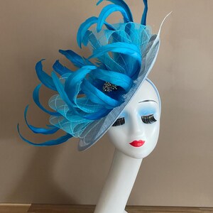 May include: A light blue fascinator with a large blue feather plume and a small jeweled embellishment.