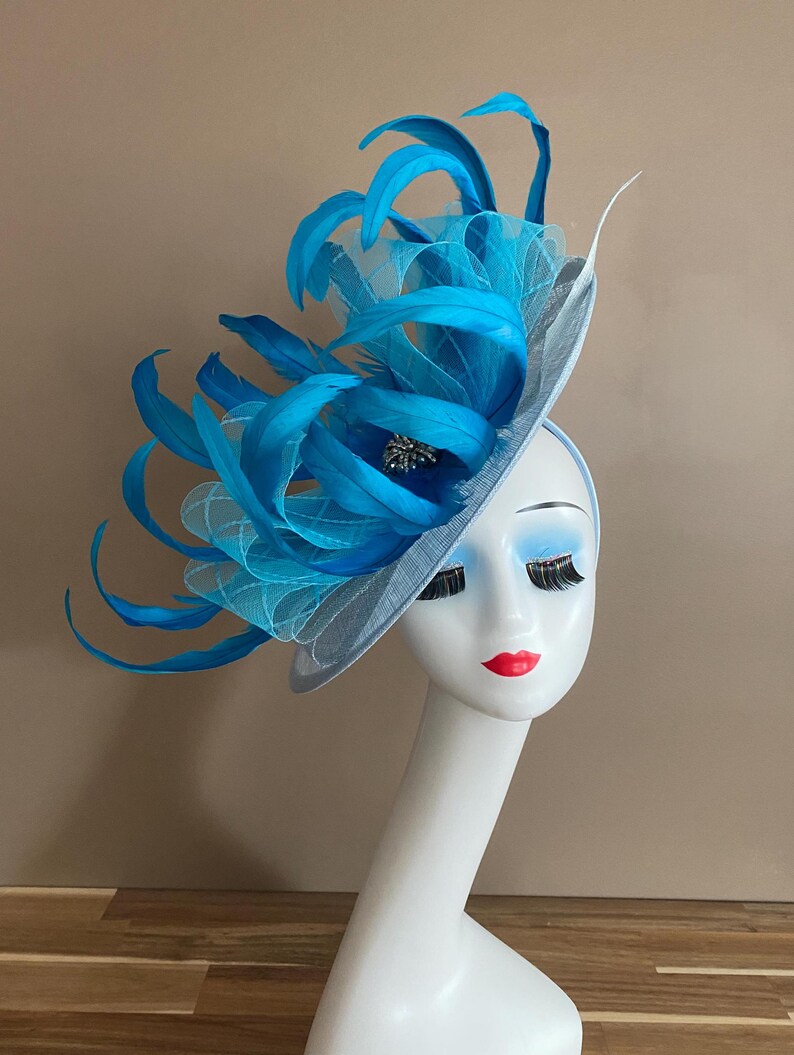 May include: A light blue fascinator with a large blue feather plume and a small jeweled embellishment.