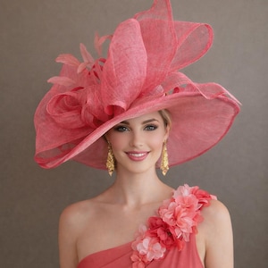Op de afbeelding: Een vrouw draagt een grote, roze hoed met een brede rand en een bloemmotief. De hoed wordt gecombineerd met een bijpassende jurk met één schouder en bloemaccenten. Gouden oorbellen maken de look compleet. De algehele esthetiek is elegant en formeel.