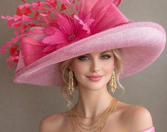 May include: A pink wide-brimmed hat with a large bow and floral accents. The hat is adorned with red and pink feathers. The woman is wearing gold earrings and a multi-strand gold necklace. She is also wearing a pink off-the-shoulder dress.