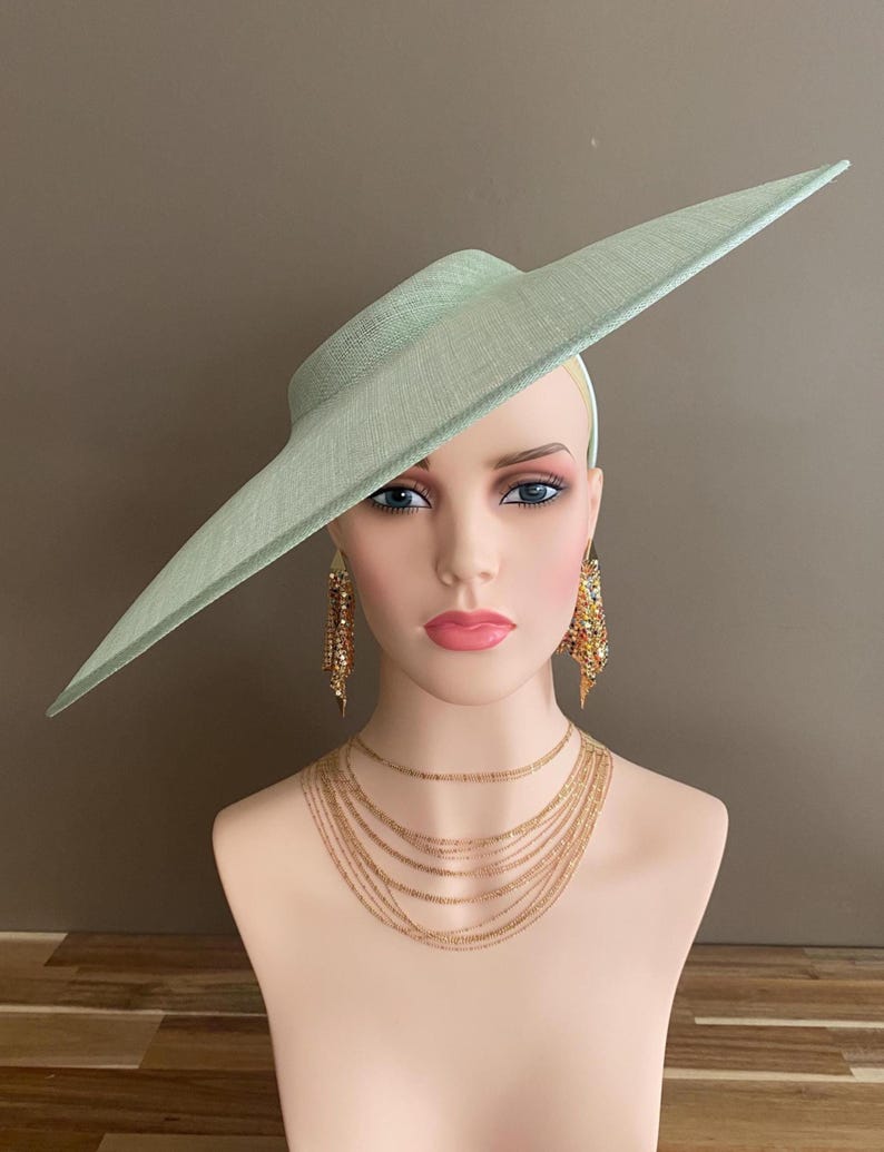 May include: A mint green hat with a wide brim, displayed on a mannequin head. The hat is paired with gold-colored layered necklaces and dangling earrings. The mannequin has a fair complexion and is set against a neutral background.