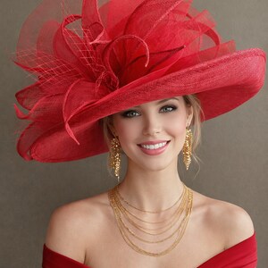 May include: A woman wearing a vibrant red hat with a wide brim and elaborate floral and netting accents. She is also wearing gold earrings and a layered gold necklace, and a red off-the-shoulder dress.