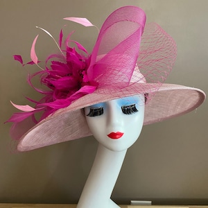 May include: A pink wide-brimmed hat with a large pink and white feather embellishment. The hat is made of a soft, textured fabric and has a wide brim that can be styled in a variety of ways.