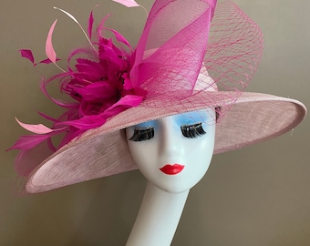 May include: A pink wide-brimmed hat with a large pink and white feather embellishment. The hat is made of a soft, textured fabric and has a wide brim that can be styled in a variety of ways.
