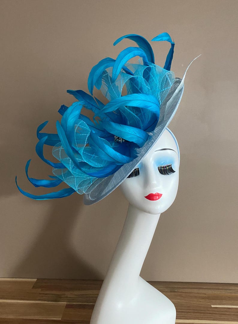 May include: A light blue hat with a large turquoise feather embellishment. The hat is made of a delicate, sheer fabric and is perfect for a special occasion.