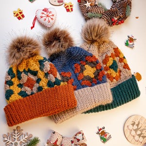 May include: Three handmade crochet hats with faux fur pom-poms. The hats feature a colorful granny square design in shades of yellow, orange, blue, and green. A Christmas wreath and decorative ornaments are also visible.