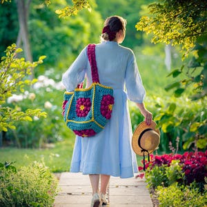 Könnte beinhalten: Eine Person geht auf einem Steinweg in einem Garten, trägt einen Strohhut und eine große, farbenfrohe Häkeltasche. Die Tasche ist türkis mit rosa und gelben Blumenmustern. Die Person trägt ein hellblaues Kleid.