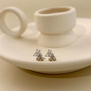 Peut inclure: Une paire de boucles d'oreilles en or avec trois petites pierres claires disposées en forme de triangle.