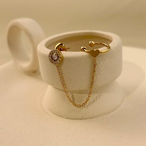 May include: Gold ear cuff with a small heart charm and a dangling chain with a round crystal-encrusted earring.