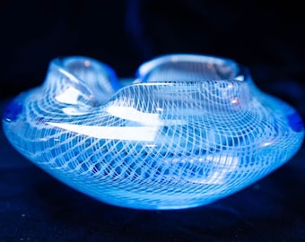May include: A blue glass bowl with a white lattice design. The bowl has a wavy, organic shape.