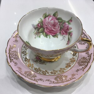 May include: A pink teacup and saucer set with a floral design. The cup and saucer are decorated with gold trim and a pink rose pattern.