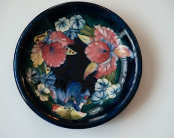 May include: A blue ceramic bowl with a floral design. The bowl features a variety of flowers in shades of pink, blue, white, and yellow. The flowers are arranged in a circular pattern around the centre of the bowl.
