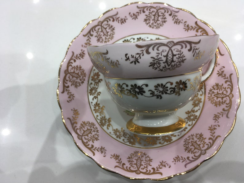 May include: A pink and white teacup and saucer set with gold trim and floral designs.