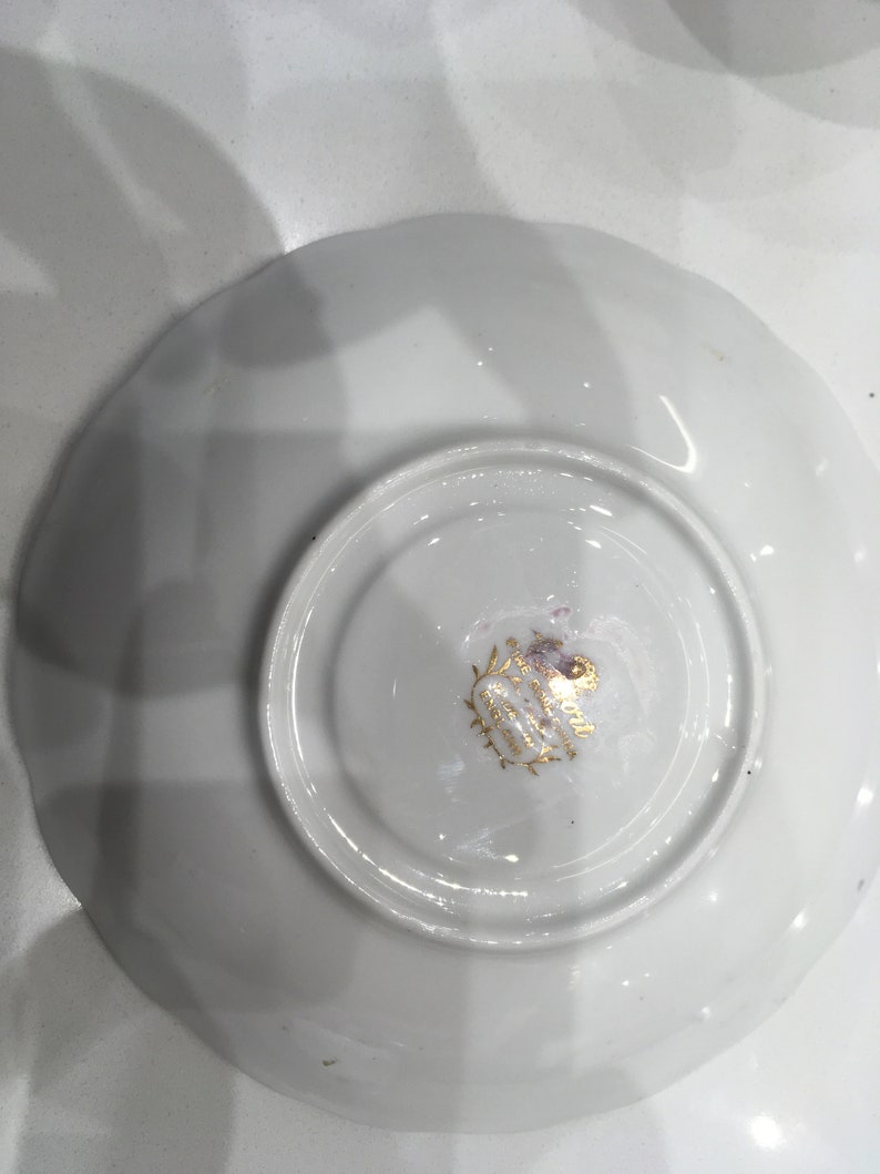 May include: White porcelain saucer with a gold rim and a gold logo that reads "Royal Albert England" and "Made in England".