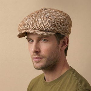 May include: A brown and white herringbone pattern newsboy cap. The cap has a rounded crown and a small, stiff brim. The cap is made of a textured fabric. The person is wearing a green shirt.