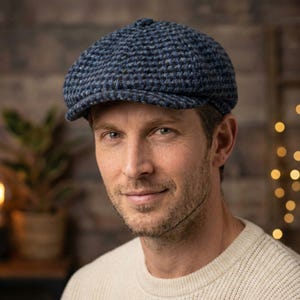 May include: A blue and black tweed newsboy cap. The cap has a rounded crown and a short, stiff brim. The cap is made of a textured fabric and is worn by a person wearing a cream-colored sweater.