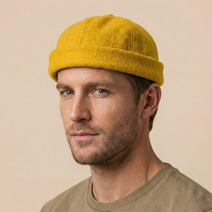 May include: Mustard yellow beanie hat. The hat is made of a soft, textured material and has a rounded crown and a folded brim. The hat is worn by a person with a neutral background.
