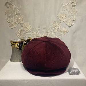 Peut inclure: Une casquette de newsboy en velours c&ocirc;tel&eacute; bordeaux avec une couronne arrondie et une visi&egrave;re plate.