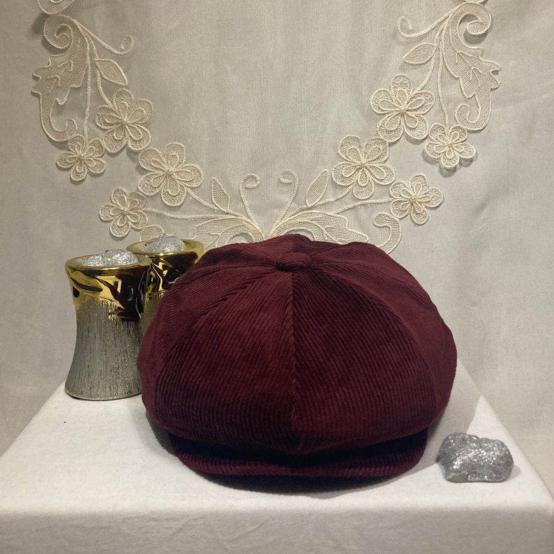 Peut inclure: Une casquette de newsboy en velours c&ocirc;tel&eacute; bordeaux avec une couronne arrondie et une visi&egrave;re plate.