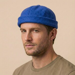 Peut inclure: Un bonnet bleu vif avec un bord roulé. Le chapeau est fait d'un tissu doux et texturé. Le chapeau est porté par une personne. L'arrière-plan est de couleur neutre.