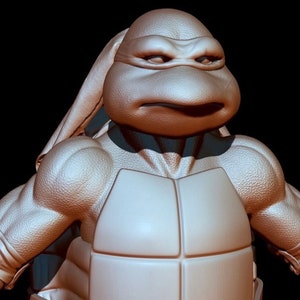 May include: A close-up of a 3D model of a Teenage Mutant Ninja Turtle, showing the head and upper body. The turtle is wearing a brown bandana and has a serious expression on its face. The turtle is sculpted in a realistic style, with detailed muscle definition and a textured shell.