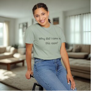 May include: A light green t-shirt with the text "Why did I come in this room?" in black. The shirt is paired with blue jeans.