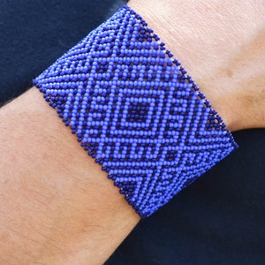 Może przedstawiać: Bransoletka z niebieskich i fioletowych koralików z geometrycznym wzorem.