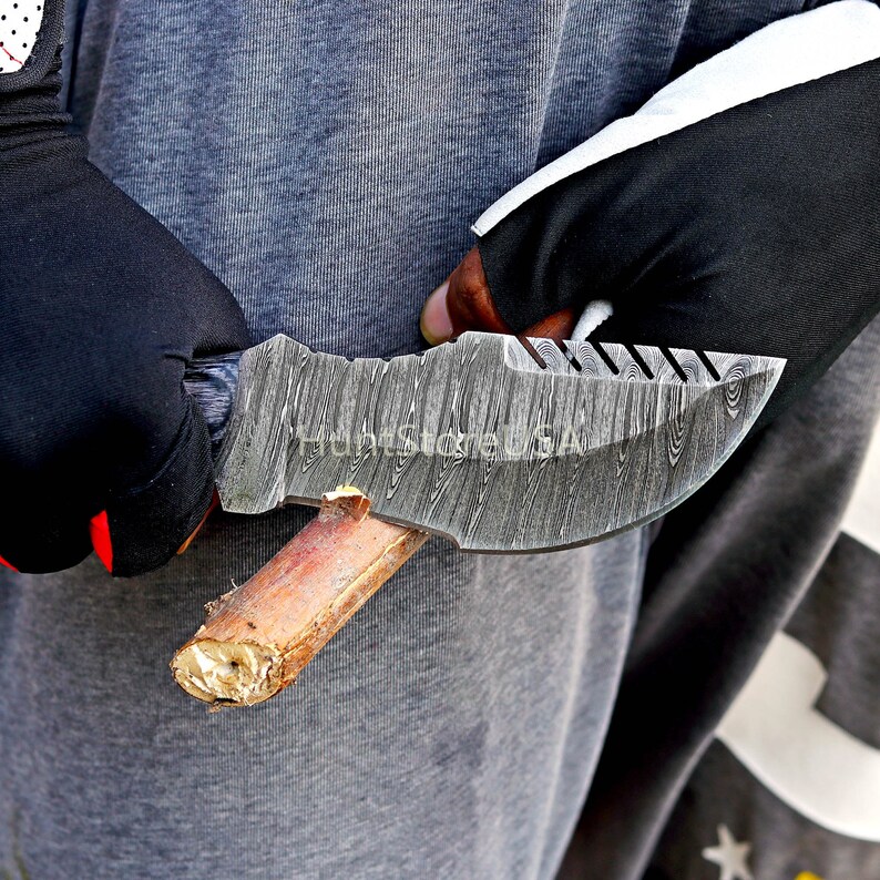 Puede incluir: Primer plano de una persona sosteniendo un cuchillo de acero Damasco con mango de madera. El cuchillo tiene una hoja texturizada y una punta afilada.