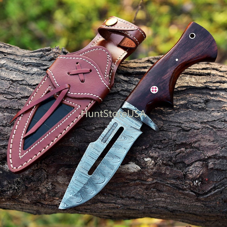 May include: A hunting knife with a brown wooden handle and a Damascus steel blade. The knife is in a brown leather sheath with a strap.
