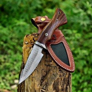 May include: A Damascus steel hunting knife with a wooden handle and a leather sheath. The knife is sharp and has a distinctive pattern on the blade.
