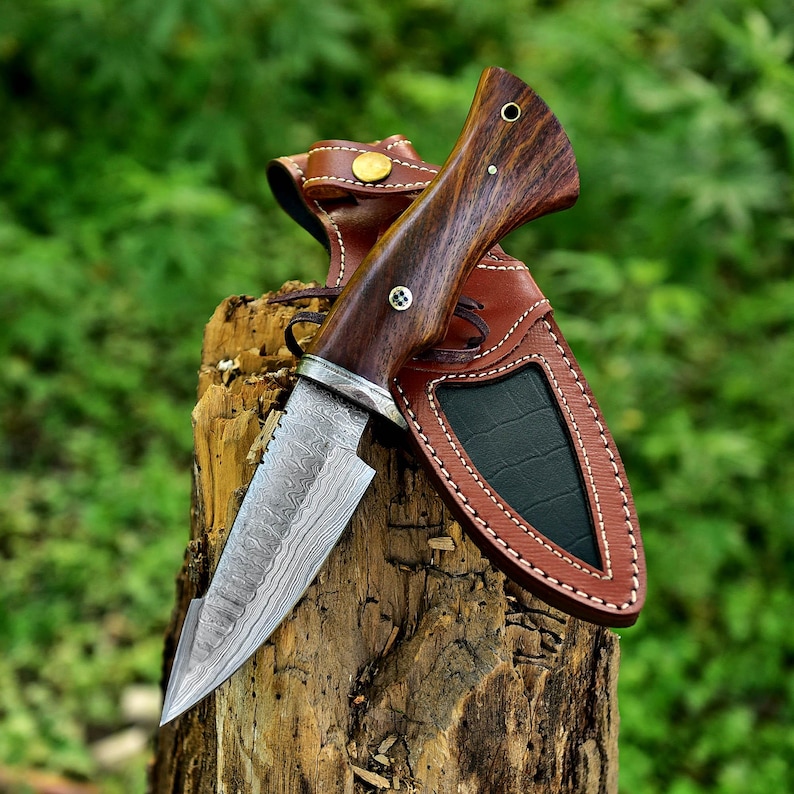 May include: A Damascus steel hunting knife with a wooden handle and a leather sheath. The knife is sharp and has a distinctive pattern on the blade.