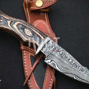 May include: A black and brown wood handle knife with a Damascus steel blade. The knife is in a brown leather sheath.