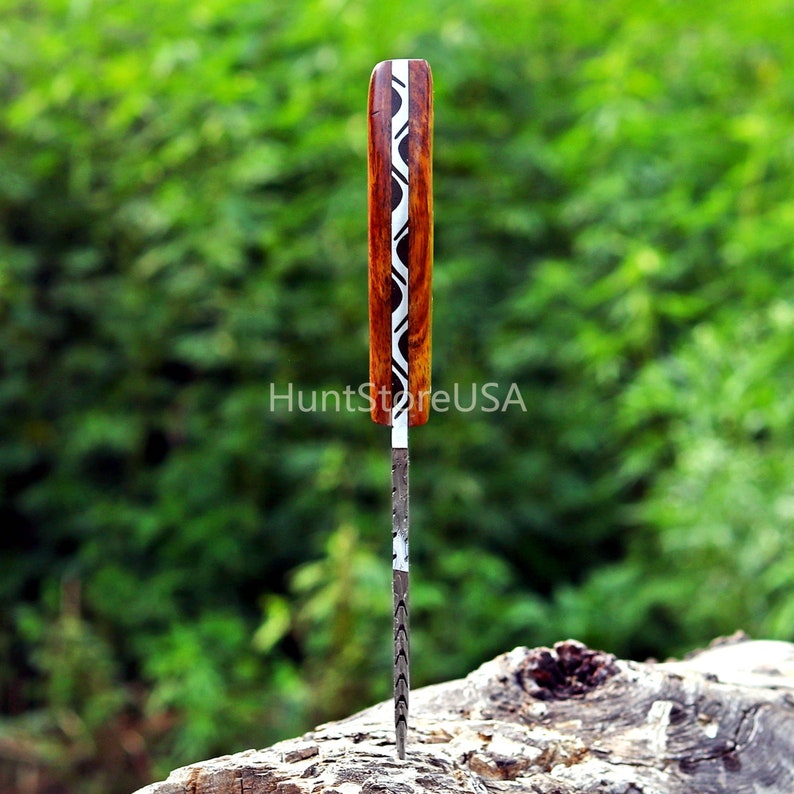 Puede incluir: Primer plano de un cuchillo con mango de madera con un patr&oacute;n ondulado en blanco y negro. El cuchillo est&aacute; parcialmente insertado en un trozo de madera.