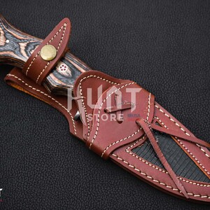 May include: A brown leather sheath with a black and brown wooden handle knife. The sheath has a decorative stitching pattern and a strap with a knot.